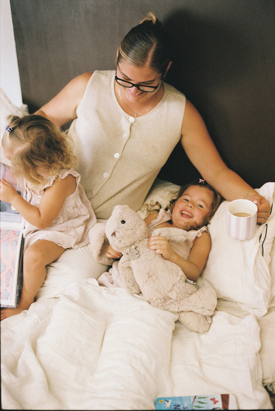Woman and two children in bed with teddy bears and a cup.