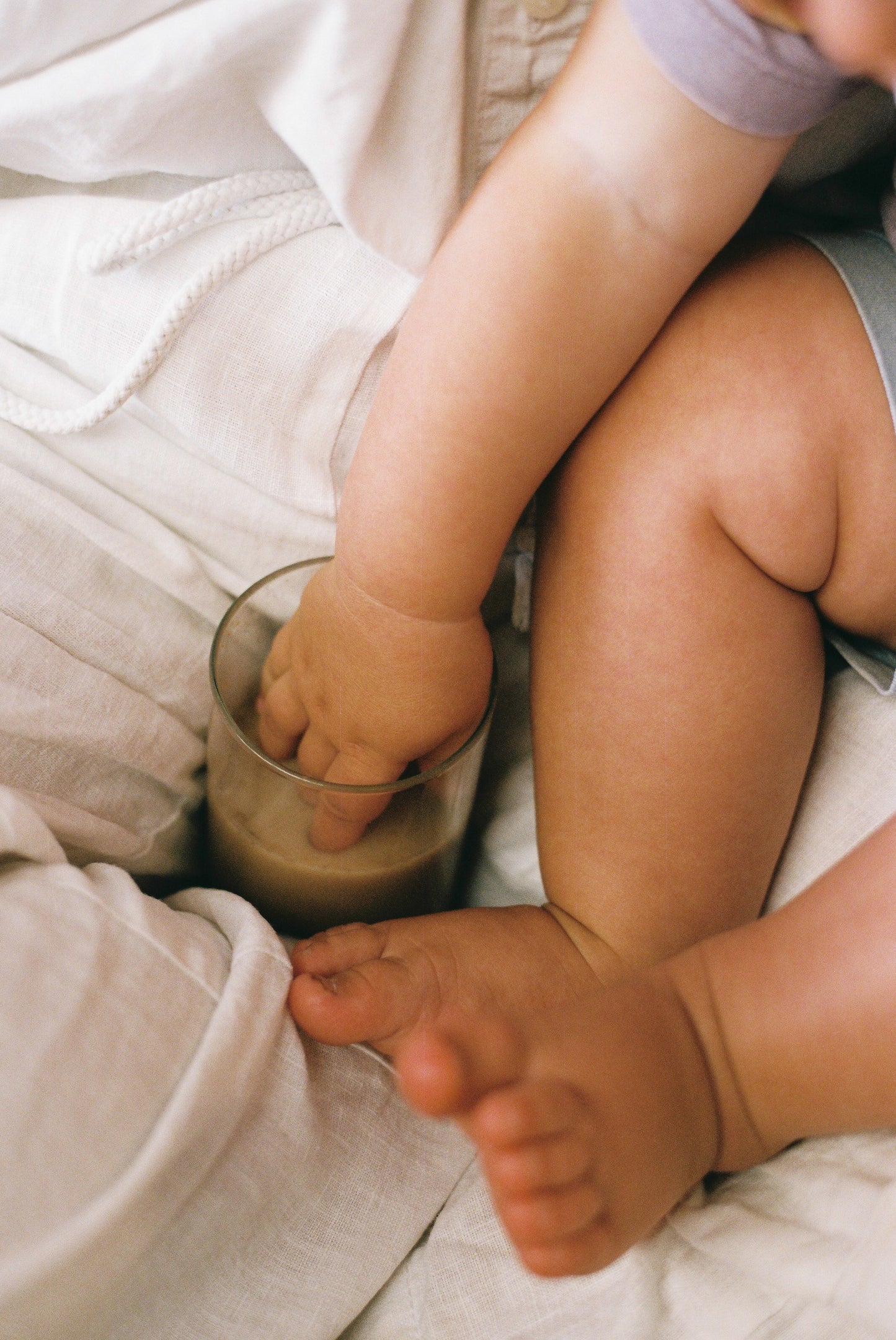 Child's hand reaching into a glass of dark liquid on a light-colored surface.