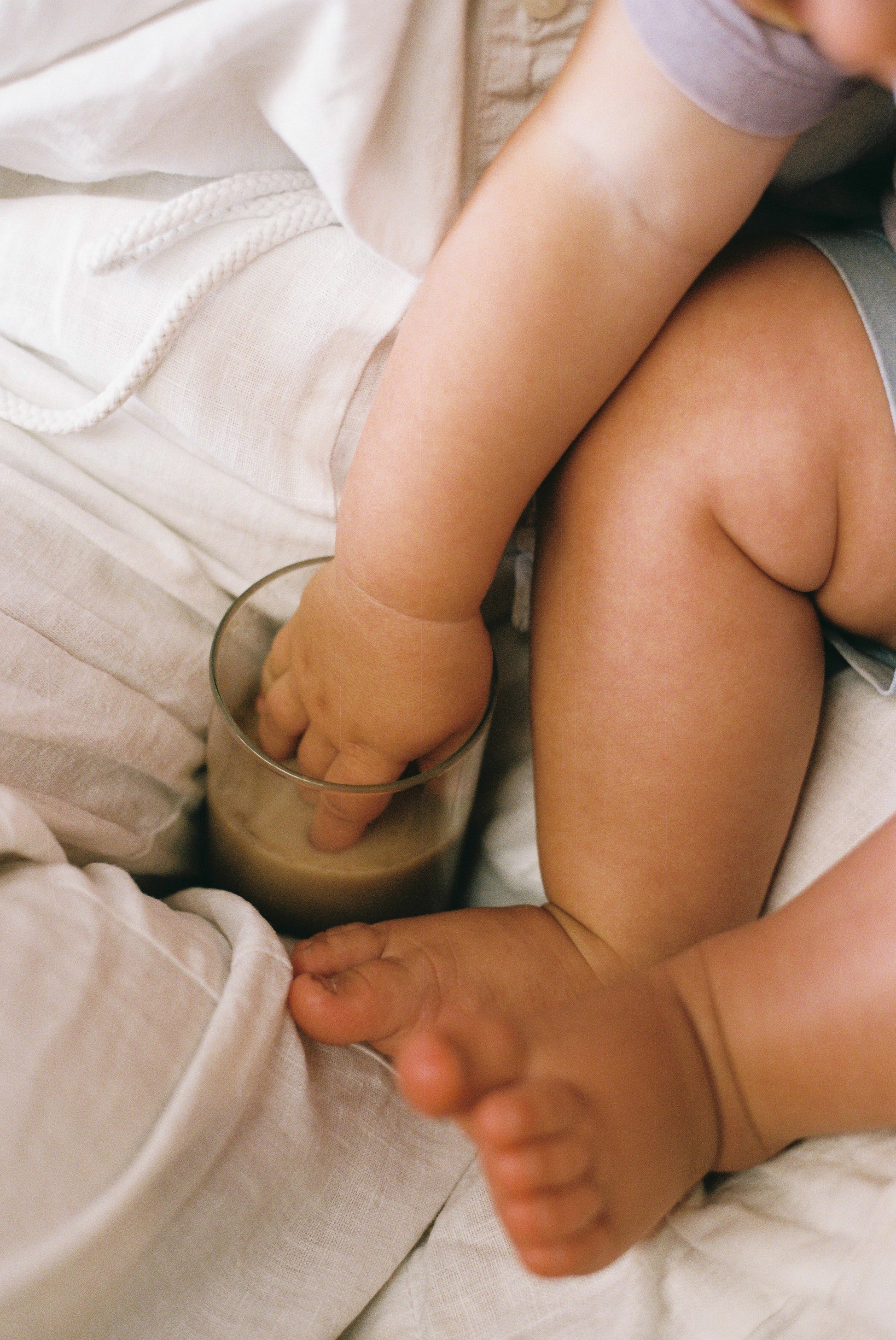 Child's hand reaching into a glass of dark liquid on a light-colored surface.
