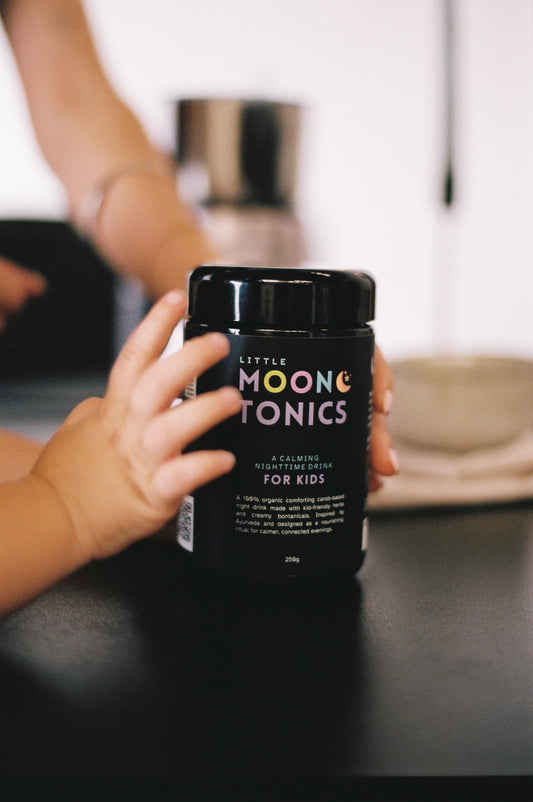 Kids hands holding a jar of Little Moon Tonics on a table