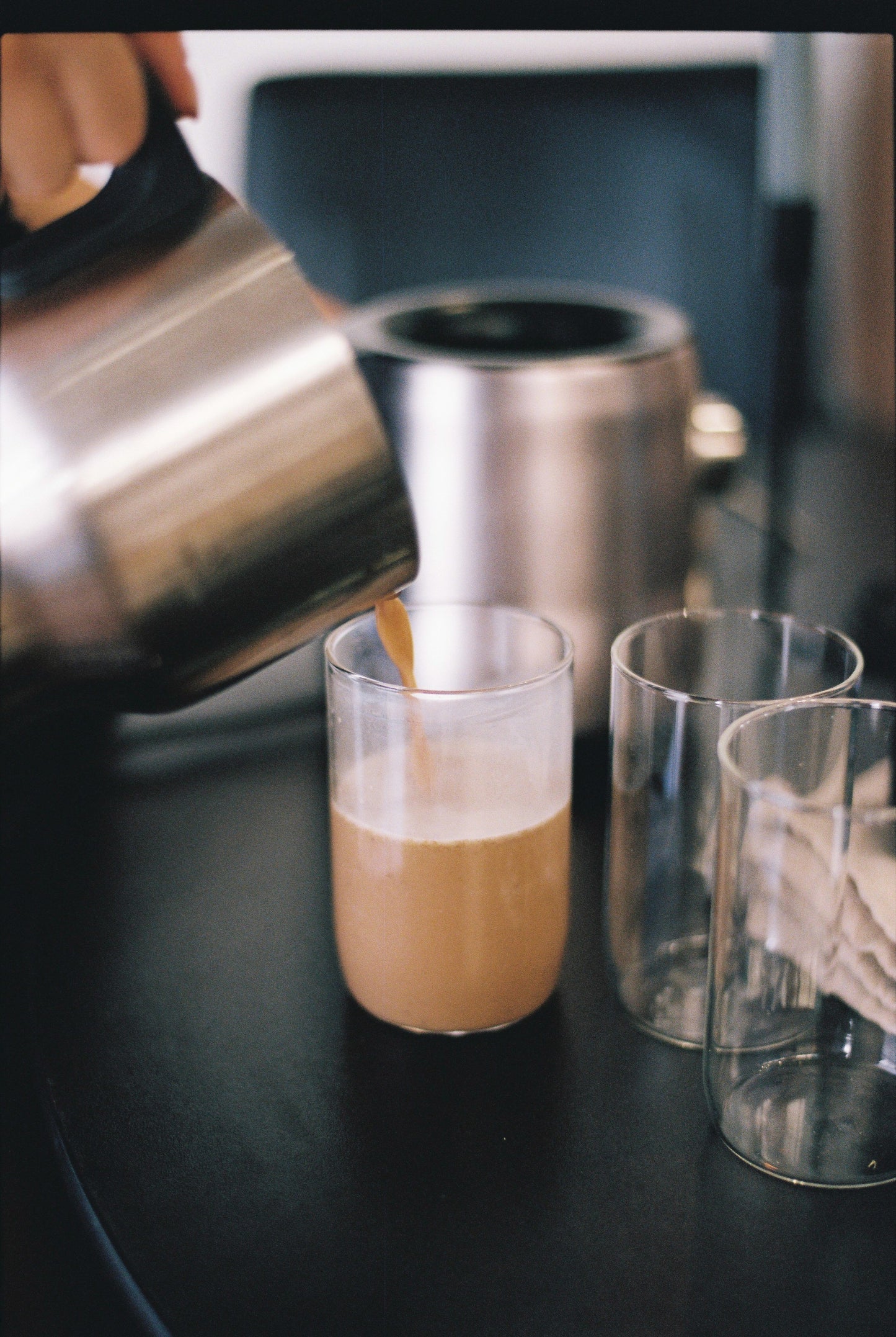 Coffee being poured into a glass on a dark surface with a blurred background